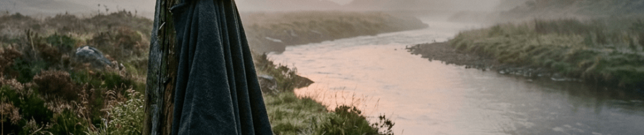 Cloak hanging on a wooden post by a river with misty mountains in the background at sunrise