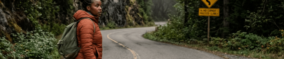 Person wearing orange jacket and backpack walking across a curvy forest road